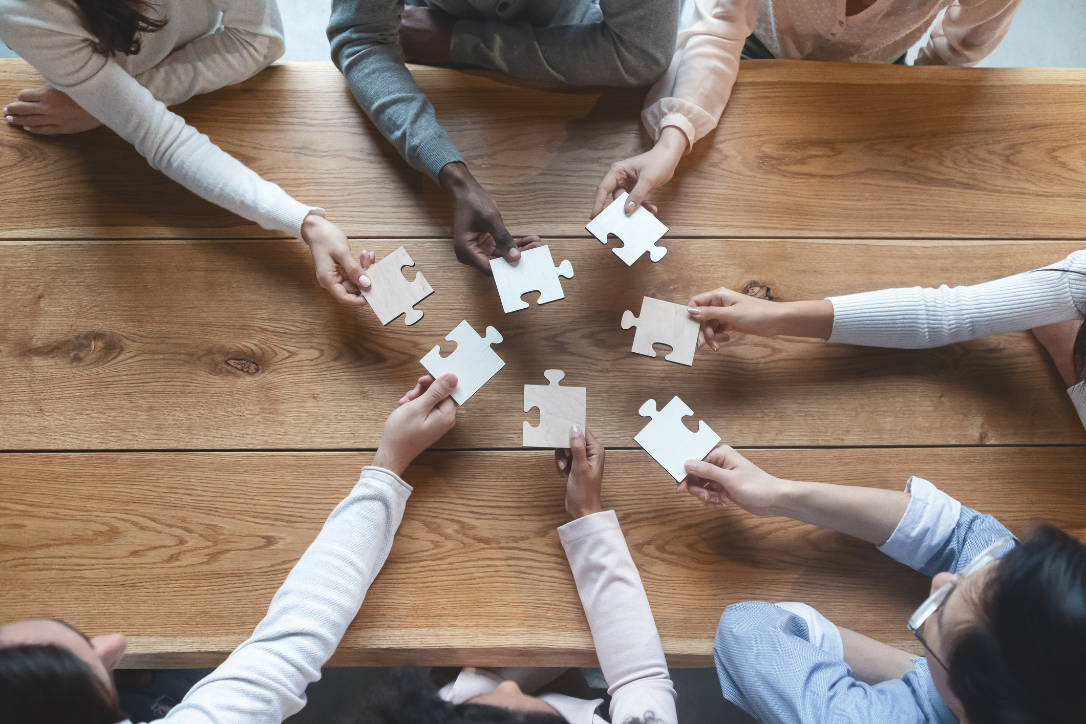 Photo of multiple hands in a circle holding puzzle pieces towards the centre of a table