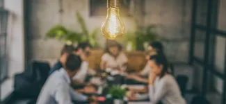 Photo of researchers in discussion at a table with a bright light bulb overhead