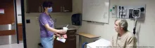 Photo of nurse handing cup of water to patient sitting on exam bed