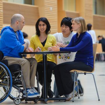 Photo of health mentor in a wheelchair and students talking at a table