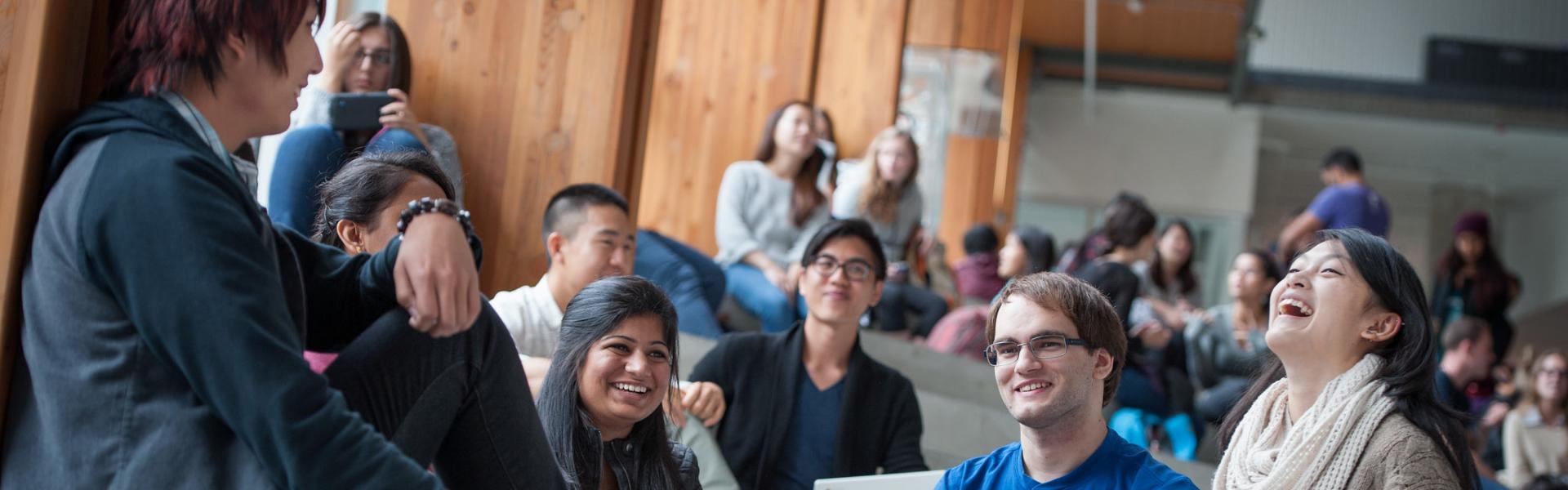 Students sitting on steps inside a UBC building discussing and laughing